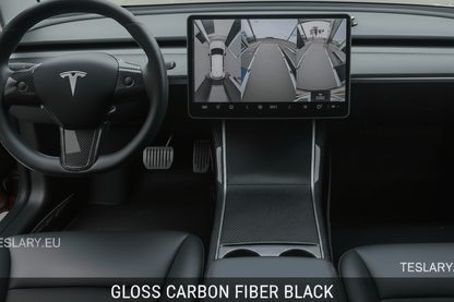 A Tesla vehicle interior showing the dashboard, steering wheel with the Tesla logo, center console, and a large infotainment screen displaying a 3D car view. Text at the bottom reads 'GLOSS CARBON FIBER BLACK' and 'TESLARY.
