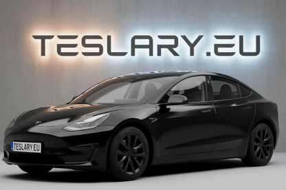 A black Tesla Model Y sedan shown from a three-quarter front angle, parked in front of a gray wall with a glowing TESLARY.EU sign and a license plate reading TESLARY EU. tesla-model-3-18-arachnid-style-wheel-covers-teslary-dublin-ireland-cork-nederlands-deutschland-espana-alicante-madrid-tesla-accessories-shop-europe-france-ital-4448983